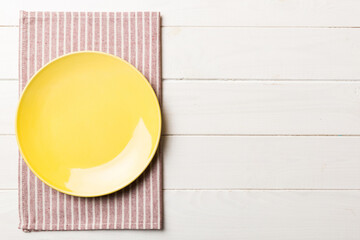 Poster - Top view on colored background empty round yellow plate on tablecloth for food. Empty dish on napkin with space for your design