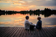 © luengo_ua - Romantic holiday. Senior loving couple sitting together on lake bank enjoying beautiful sunset.