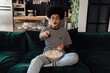 © Drobot Dean - Shocked african woman watching tv and eating popcorn while sitting on couch