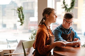 Wall Mural - Woman training man with down syndrome to work in cafe while sitting at table