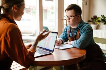 Woman using laptop while training man with down syndrome to work in cafe