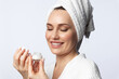 © deniskomarov - Beautiful, stylish, middle-aged smiling woman with a towel on her head, holding a jar of skin moisturizer cream