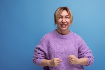 Sticker - energetic blond young woman in purple hoodie on blue background with copy space