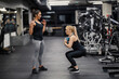 © Dusan Petkovic - A female personal trainer is showing exercises to a sportswoman who is squatting and holding kettlebell in a gym.