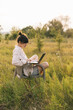 © Ananass - a young woman wearing a shirt works on a laptop while sitting on a chair in the middle of nature
