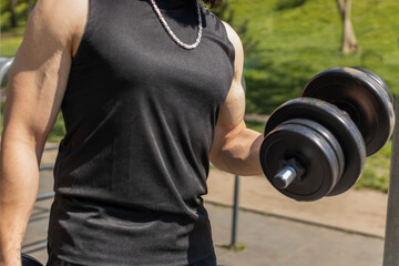 Close-up athletic man in sportswear doing arms weight lifting dumbbells exercises, pumping up arm bicep muscles. Guy on playground. Sports, fitness routine, bodybuilding workout. Strength motivation