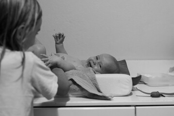 Wall Mural - A big sister making her baby sister laugh during diaper change time