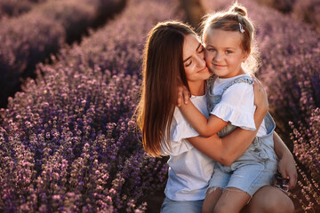 Happy family in purple lavender field. young beautiful mother and child Girl enjoy walking blooming meadow on summer day. Mom having fun with pretty daughter in nature on sunset. mothers day