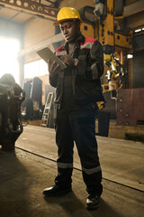 Wall Mural - Young African American male technician looking through online manual while standing in front of camera and preparing for machine repair