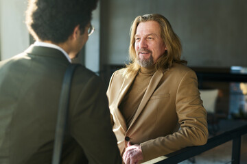 Poster - Focus on smiling mature businessman talking to young multi-ethnic male colleague during negotiation at working meeting in office center