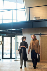Poster - Two mature colleagues in quiet luxury attire discussing working points while walking along spacious corridor or lounge in business center