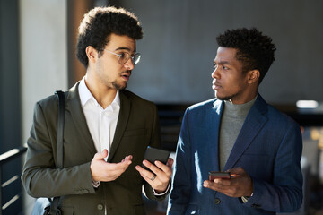 Aufkleber - Young elegant black man listening to comment of multi-ethnic male colleague explaining something in his smartphone at meeting