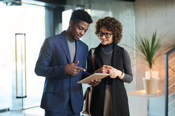 Sticker - Young confident African American manager pointing at tablet screen while making presentation of new project points to female colleague