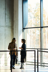 Sticker - Outlines of two mature colleagues discussing project points while standing in sunlit corridor of office center between window and railing