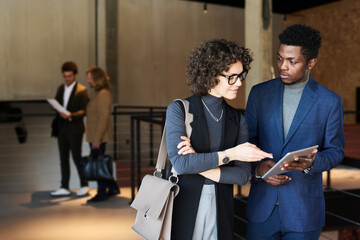 Wall Mural - Young businessman with tablet looking at female colleague pointing at screen while explaining online data during discussion of working points