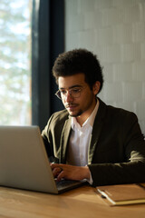 Poster - Young serious male broker or solopreneur typing on laptop keyboard and looking at screen while sitting by workplace and organizing work
