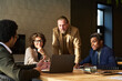 © pressmaster - Group of intercultural brokers looking at laptop screen and listening to young male colleague explaining project points during presentation