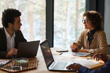 Aufkleber - Two intercultural analysts with mobile gadgets consulting about financial points at meeting in boardroom while sitting in front of one another