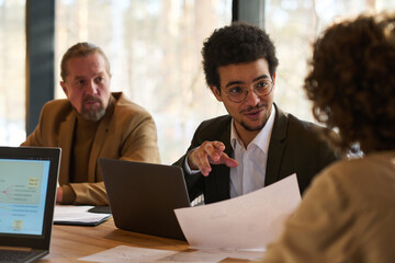 Poster - Young confident male economist with financial paper looking at female colleague during their conversation at meeting in boardroom