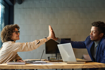 Aufkleber - Successful young male and female colleagues giving each other high-five over workplace with laptops, nobepads and paper documents