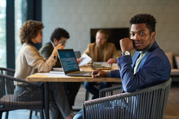 Aufkleber - Young African American chief executive officer or broker in formalwear looking at camera while sitting by workplace against group of coworkers