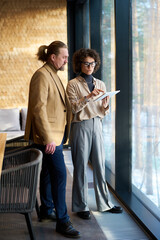 Poster - Two confident analysts looking through online financial data in tablet held by brunette businesswoman and discussing it at meeting in office