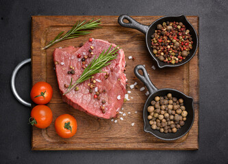 Wall Mural - Raw piece of beef with spices pepper, rosemary sprig, salt and olive oil on a wooden board, black background