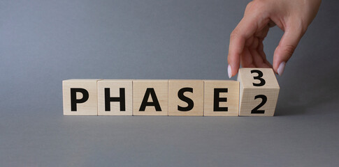 From Phase 2 to 3 symbol. Businessman Hand turns cubes and changes words Phase 2 to Phase 3. Beautiful grey background. Business and Phase concept. Copy space