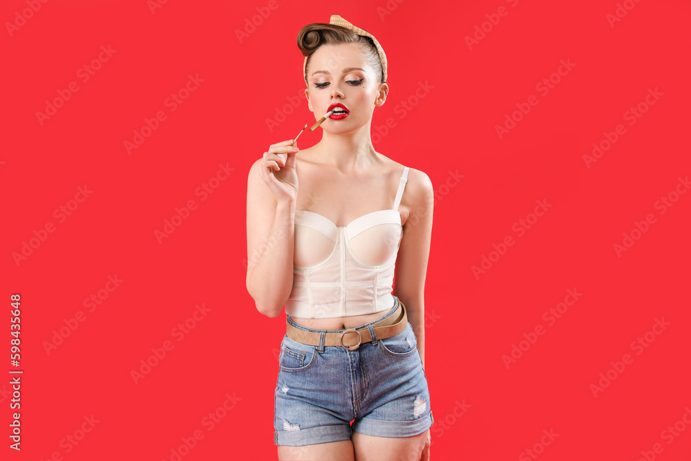 Young pin-up woman with cigarette and burning match on red background