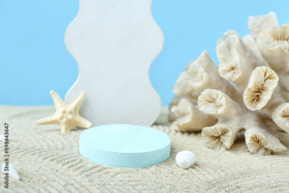Decorative plaster podiums, coral, starfish and seashells in sand on blue background
