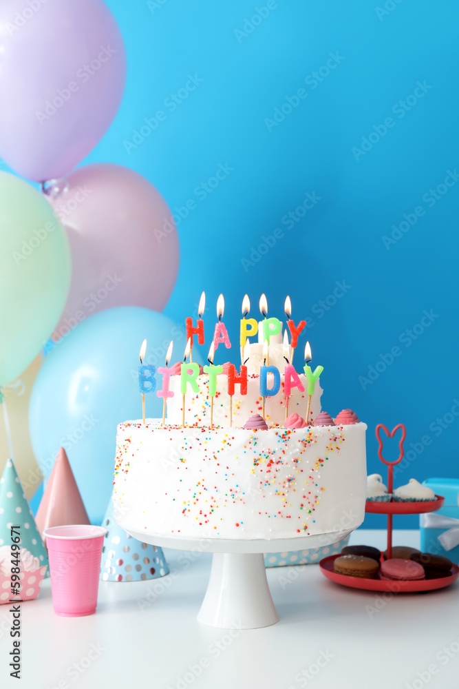 Birthday cake with different sweets on table near blue wall
