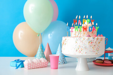 Wall Mural - Birthday cake with different sweets on table near blue wall