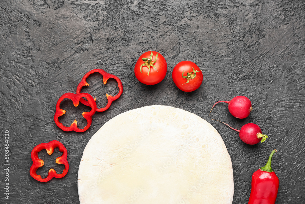 Raw dough and ingredients for preparing vegetable pie on dark grunge background