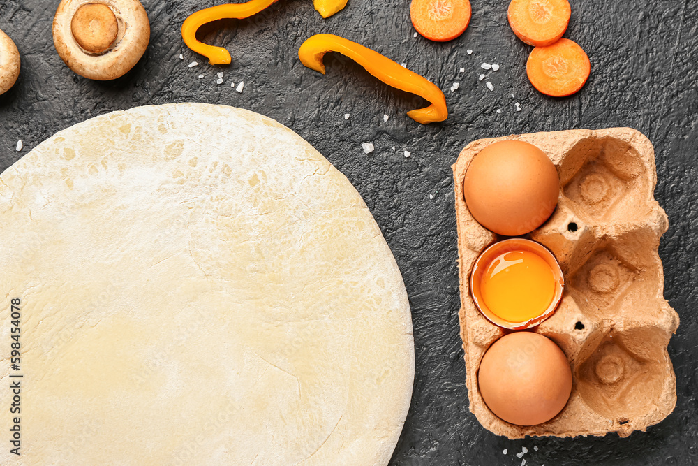 Raw dough and ingredients for preparing vegetable pie on dark grunge background