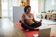 © Baba Images - Young pregnant latina woman meditating at home wihle using a laptop