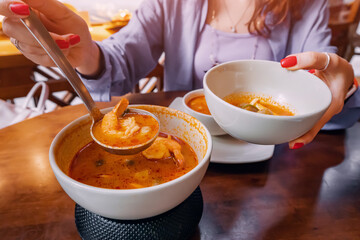 Wall Mural - Pours delicious and spicy traditional Thai Tom Yam soup with seafood on plates in the restaurant