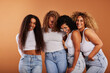 © Flamingo Images - Diverse women in white tops and jeans laughing on an orange background