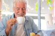 © luciano - Smiling old senior man in coffee shop having breakfast with cappuccino and sweet cake. Elderly people enjoying free lifestyle and pleasant moment of relax