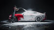 © Gorodenkoff - Car Wash Expert Using Water Pressure Washer to Clean a Red Modern Sportscar. Adult Man Washing Away Dirt, Preparing an American Muscle Car for Detailing. Creative Cinematic Photo with Luxury Vehicle