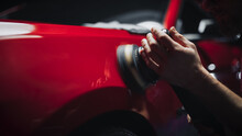 Car Ad Style Photo Of A Professional Car Detailer Using An Electric-Powered Polishing Machine To Work On A Fender Of A Beautiful Red Sportscar After Washing And Detailing The Vehicle