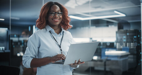 Wall Mural - Portrait of a Black Diverse Female Wearing Glasses, Using Laptop Computer, Looking at Camera and Smiling. African Information Technology Specialist, Software Engineer or Developer