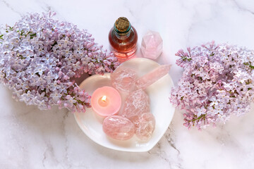 gemstones minerals, candle, essential oil bottle, lilac flowers on marble abstract background. rose quartz for Crystal ritual. spiritual Healing practice for body care, relax, meditation. top view