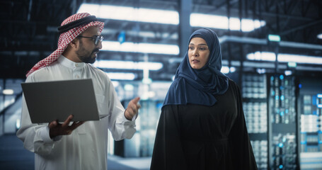 Wall Mural - Middle Eastern Computer Engineer and Cybersecurity Specialist Work in Server Facility. Muslim Female and Male Managers Talk, Perform System Maintenance Check with Laptop Computer