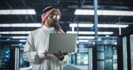 Poster - Portrait of a Middle Eastern IT System Engineer Wearing Traditional White Robe, Using Laptop Computer in a Modern Technological Server Farm Facility. Arab Artificial Intelligence Expert at Work
