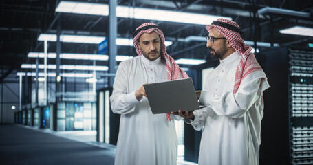 Poster - Middle Eastern Computer Engineer and Cybersecurity Professional Work in Server Room, Talk, Perform System Maintenance Check with Laptop Computer. Specialists Doing Database Diagnostics in Data Center