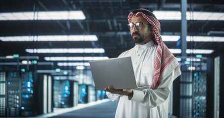 Poster - Portrait of a Muslim Data Center Technical Manager Wearing Traditional White Clothes, Using Laptop Computer in a Modern Technological Server Farm Facility. Arab Cybersecurity Expert at Work