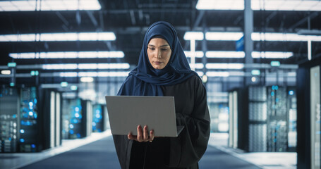 Wall Mural - Muslim Female Data Center IT Engineer Standing in a Room with Server Racks. Cloud Computing Architect Uses Laptop Computer for Servicing the System in Cyber Security and Data Protection Facility