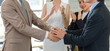 © Bangkok Click Studio - Professional successful two unrecognizable unknown businessmen in formal business suit standing holding shaking hands together after deal done while Asian female colleagues clapping hands applauding