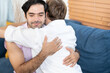 © Wongsakorn - Gay Couple Sit Together on a Sofa at Home. Boyfriends are Hugging and Embracing Each Other. A gay couple hug each other.