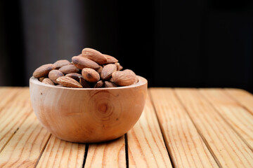 Peeled almonds in a wooden bowl and some scattered nuts on black background	
